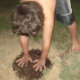 A boy bending over and pressing peat down with his hands